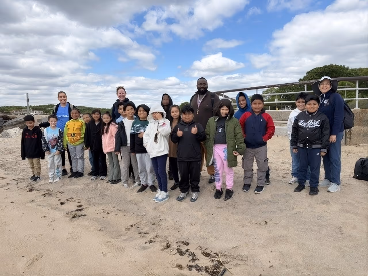 Students and teachers posing together on a sandy beach field trip