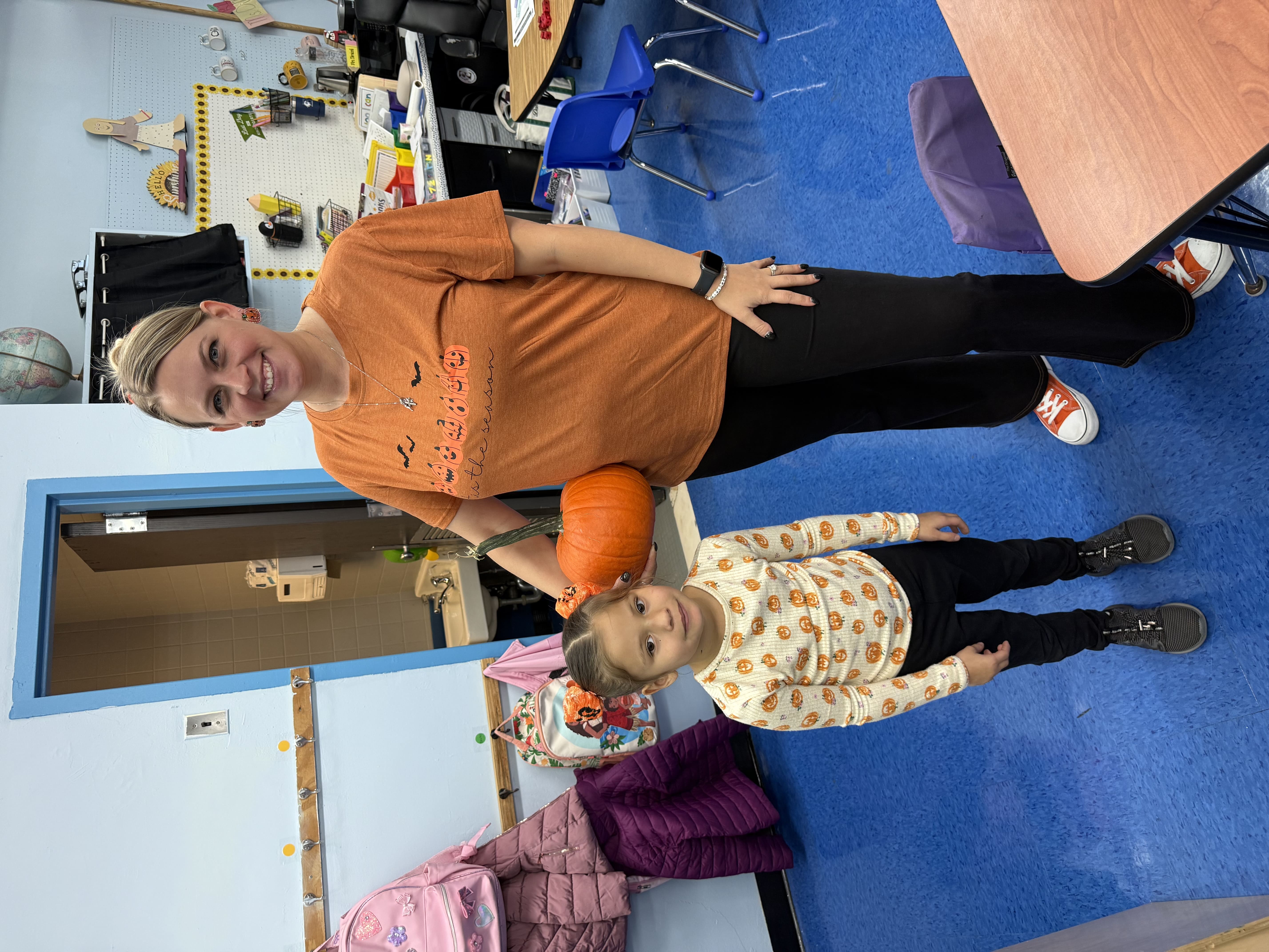PS 152 teacher holding a pumpkin beside a student in a pumpkin-print sweater