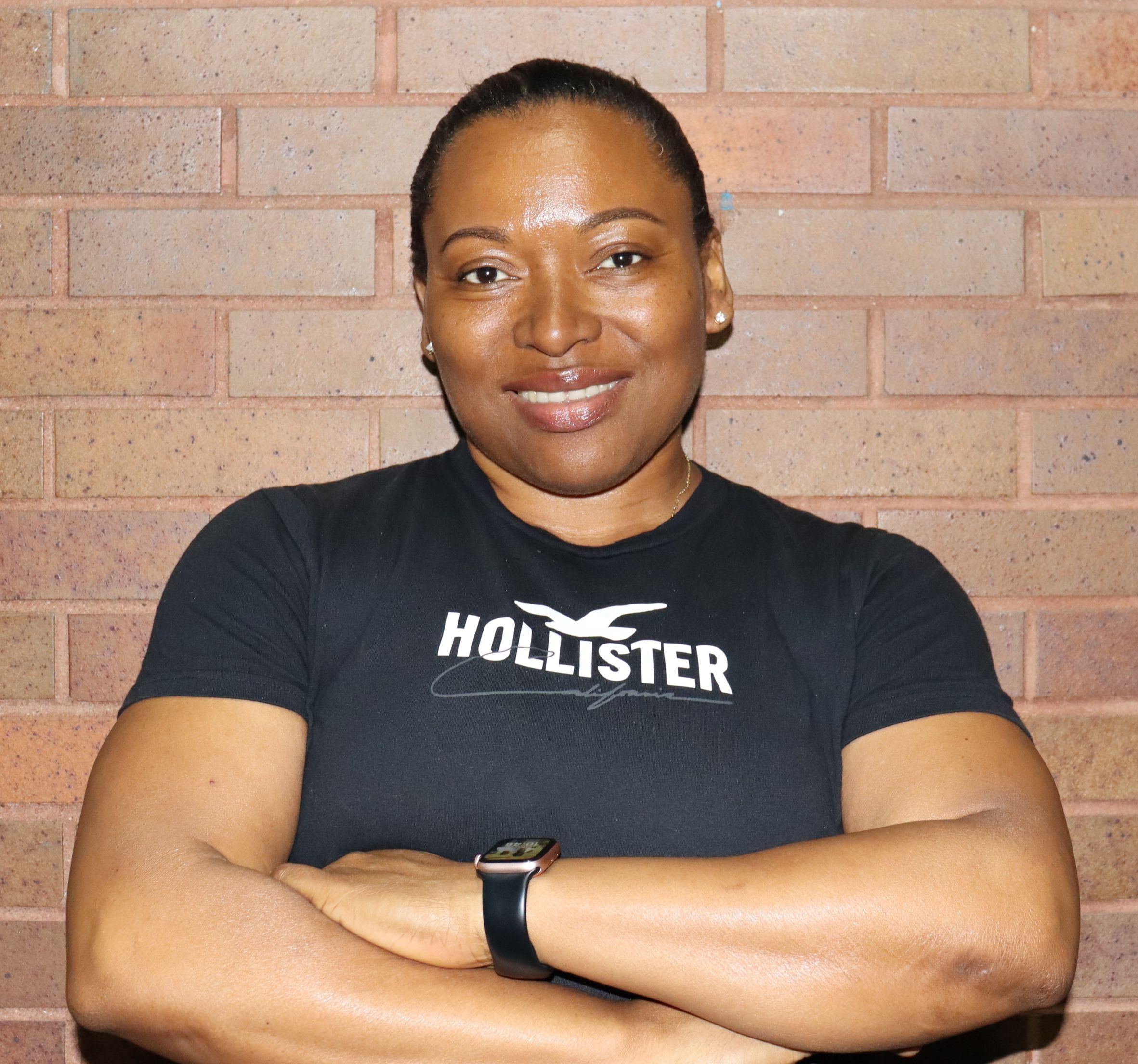 Ms. Murillo smiling with arms crossed against brick wall