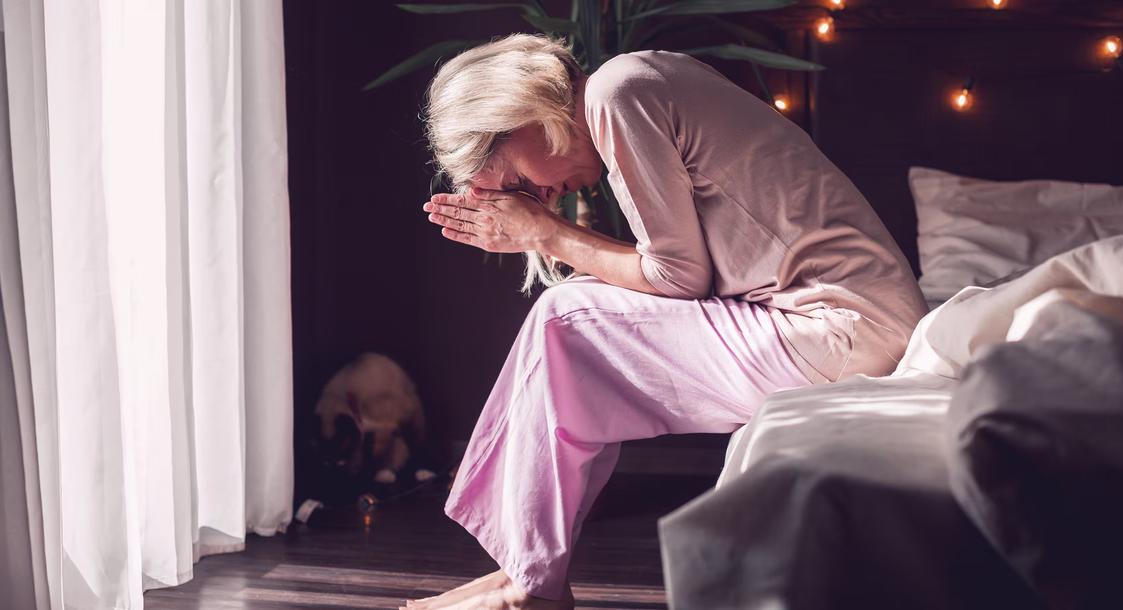 Woman sitting on her bed at home, representing frequent sleep issues and fatigue common in menopause.