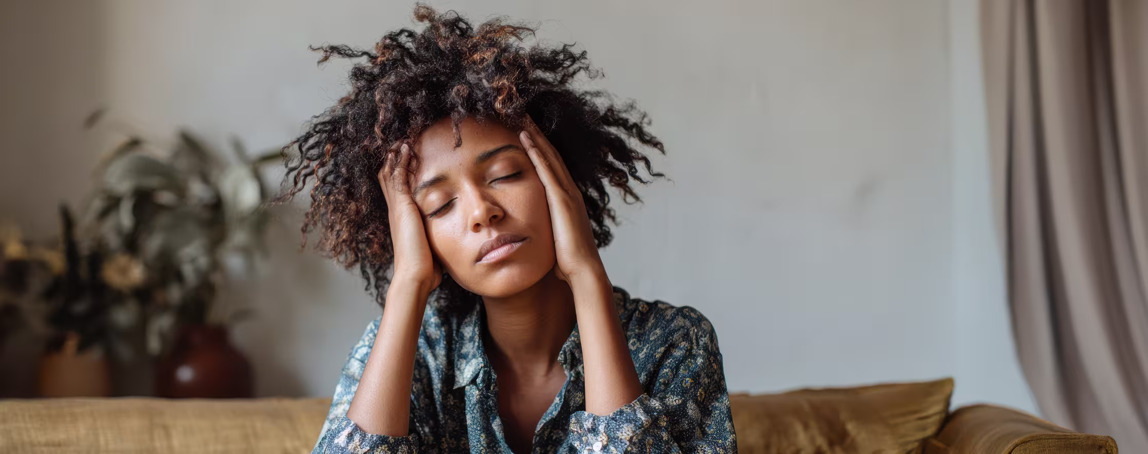 Tired Black woman sitting on a couch, experiencing emotional exhaustion, stress, and insomnia during perimenopause.