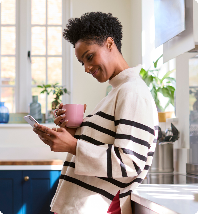 Woman standing in kitchen using smart phone.