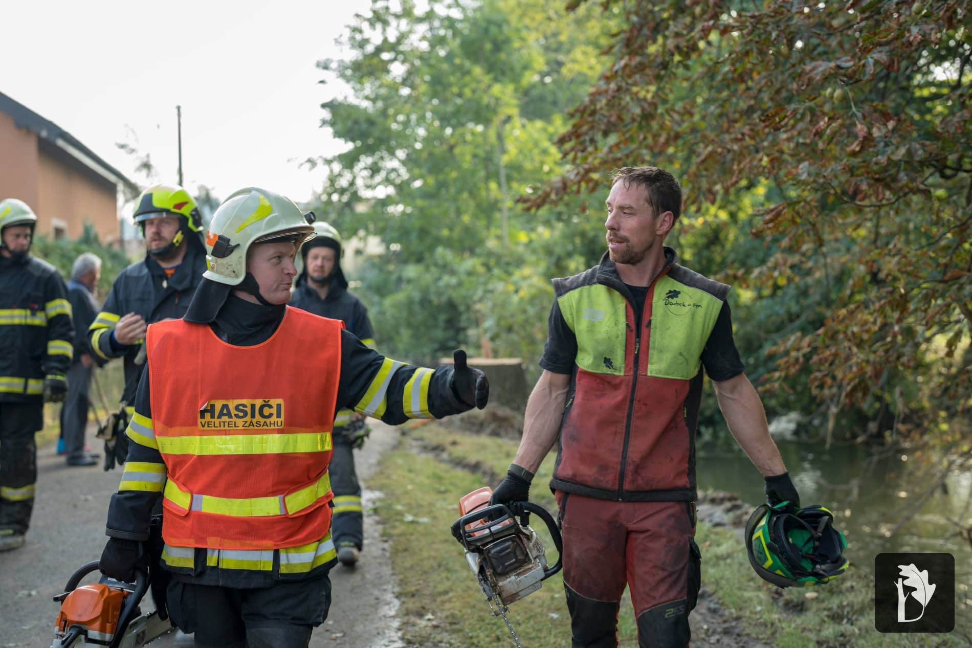 arboreta člověk s motorovou pilou jde po silnici s hasiči, kterým pomáhá při zásahu