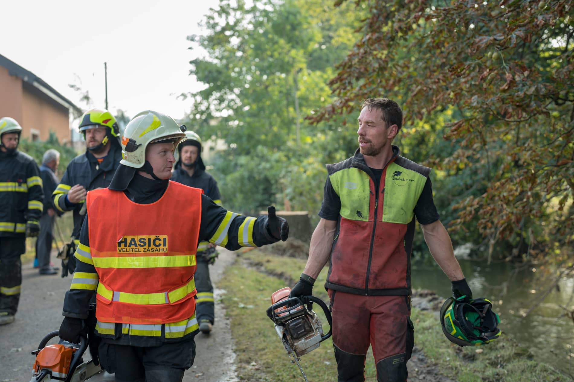 arboreta člověk s motorovou pilou jde po silnici s hasiči, kterým pomáhá při zásahu