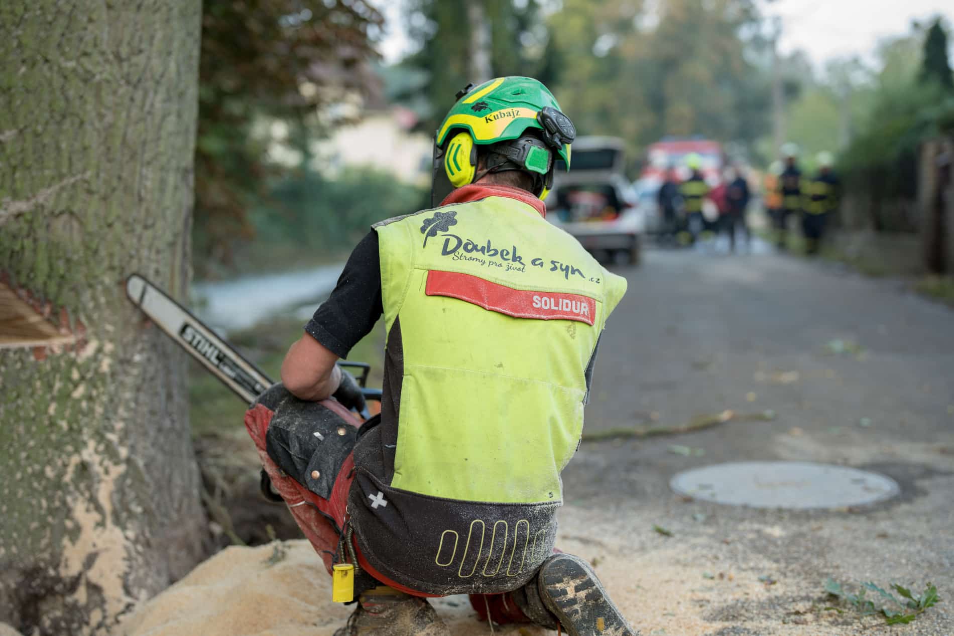 jakub firmy doubek a vnuci, pilař který kácí strom dub po povodních, který se nebezpečně naklonil nad dům, v pozadí stojí hasiči, kteří akci přihlížejí