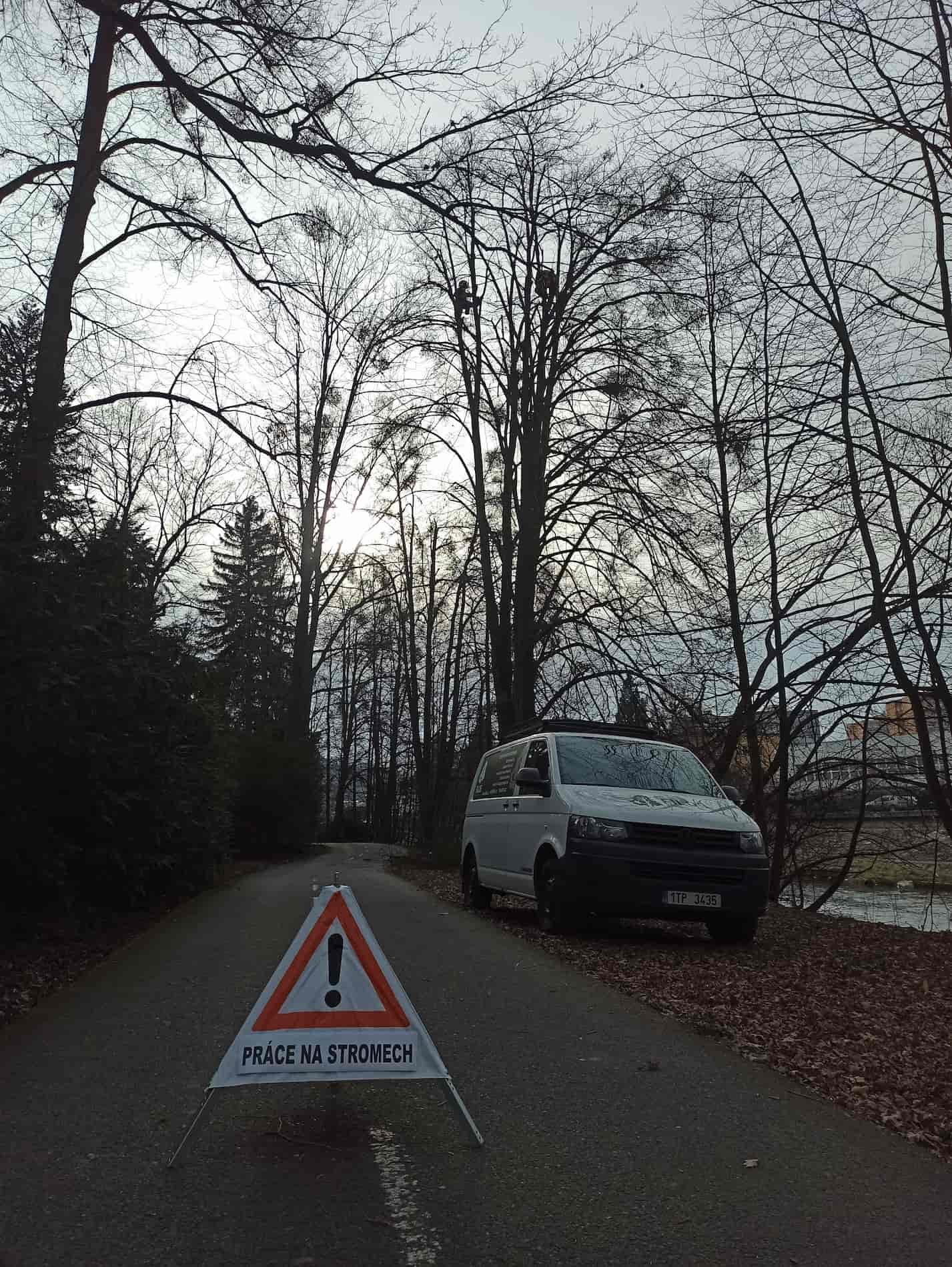 Zajištění bezpečnosti na pracovišti výstrahou na chodníku, stojícím autem a pozemním pracovníkem. na stromě je arborista
