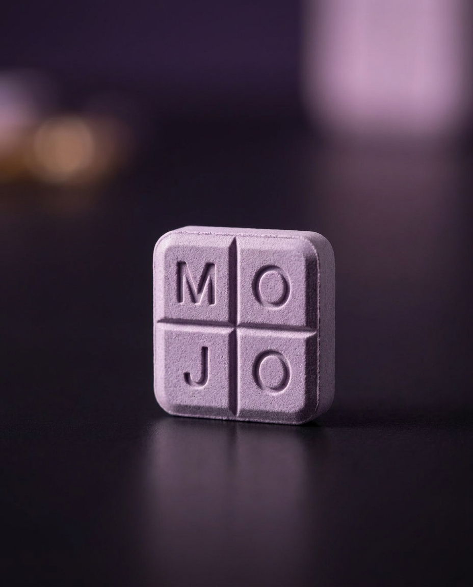 A single lavender Mint Mojo troche embossed MOJO, lit on dark slate