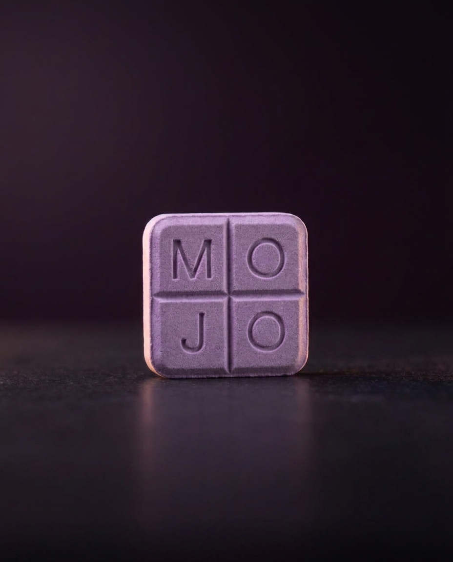 A lavender Mint Mojo troche embossed MOJO, warm rim light on dark slate