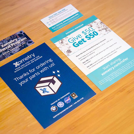A photo of the front and back views of both a referral card and referral flyer flatlaid on a bamboo tabletop
