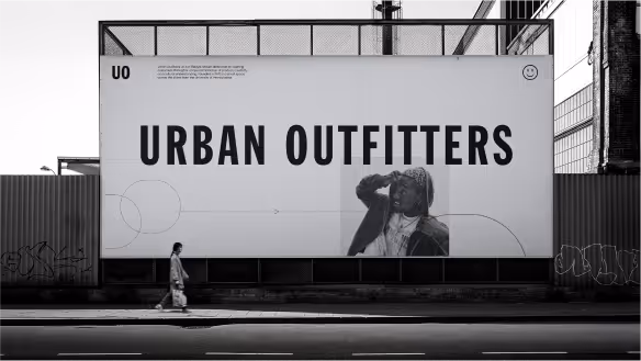 Black and white photo of a large Urban Outfitters billboard with a man walking past on the sidewalk below.