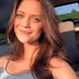 Smiling young woman with long hair sitting in car seat, sunlight on her face.
