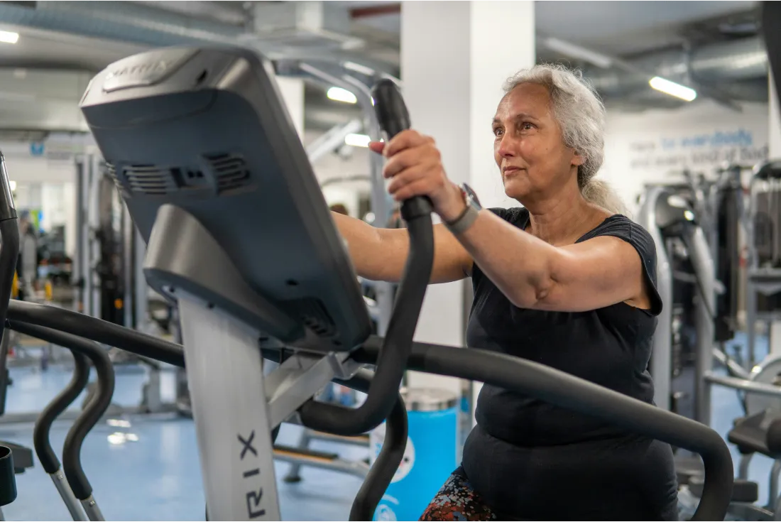 Oudere vrouw aan het sporten in een sportschool op de crosstrainer.