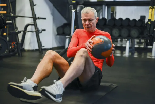 Oudere man aan het sporten met een medicine ball in een sportschool.