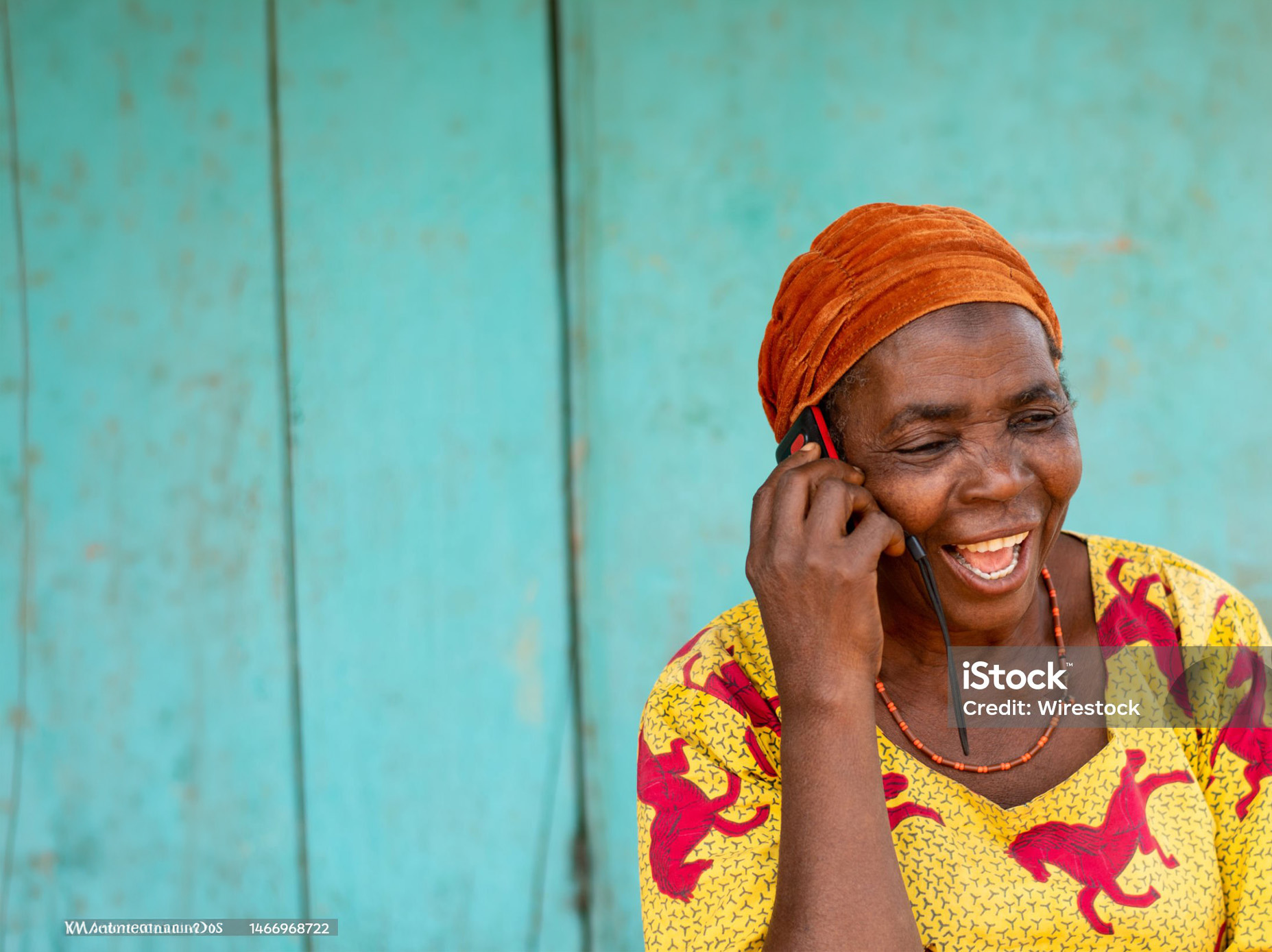 Smiling woman in a rural African setting talking on a basic mobile phone