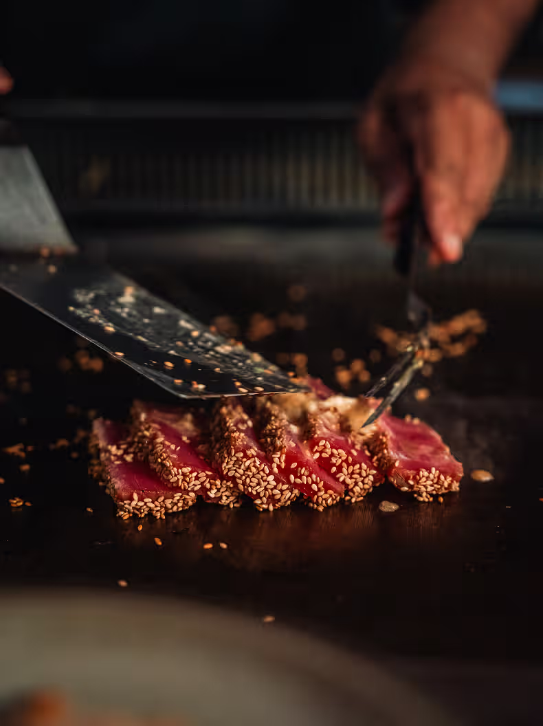 Chef slicing sesame-crusted seared tuna on a hot grill at Sekai restaurant.