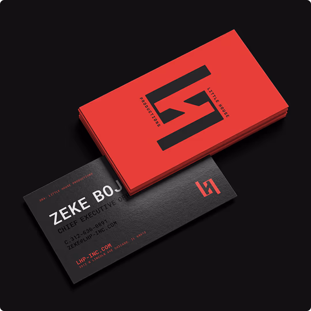 Stack of red business cards with black logo on top of a black business card showing contact details for Zeke Boj, Chief Executive Officer at Little House Productions.
