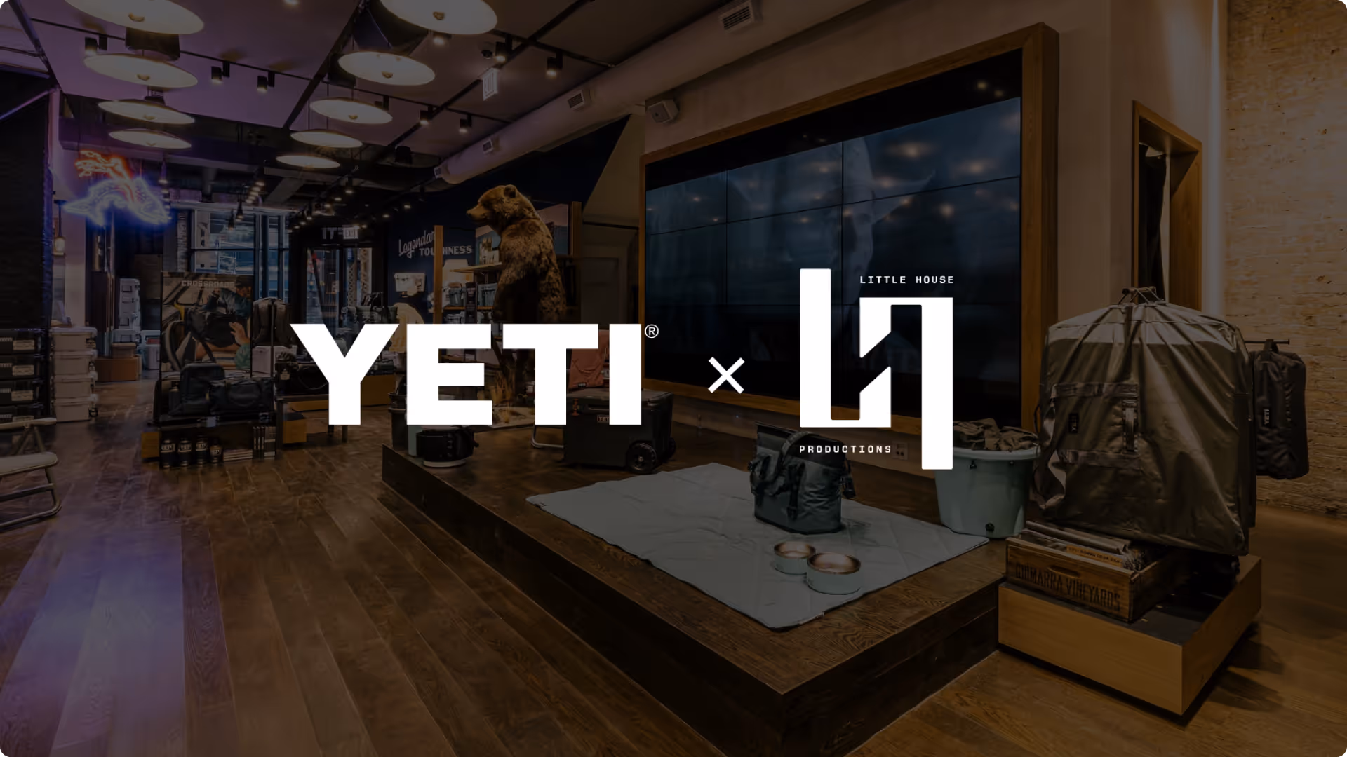 Interior of a retail store displaying Yeti brand outdoor gear, including coolers and bags, with a large bear statue and a big screen on the wall.