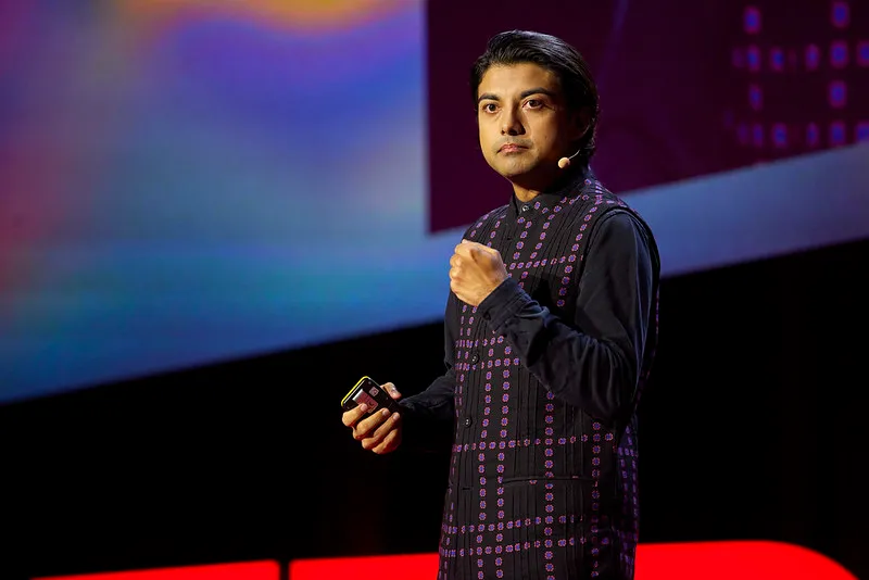 Speaker wearing a patterned vest and microphone headset delivering a presentation on stage.