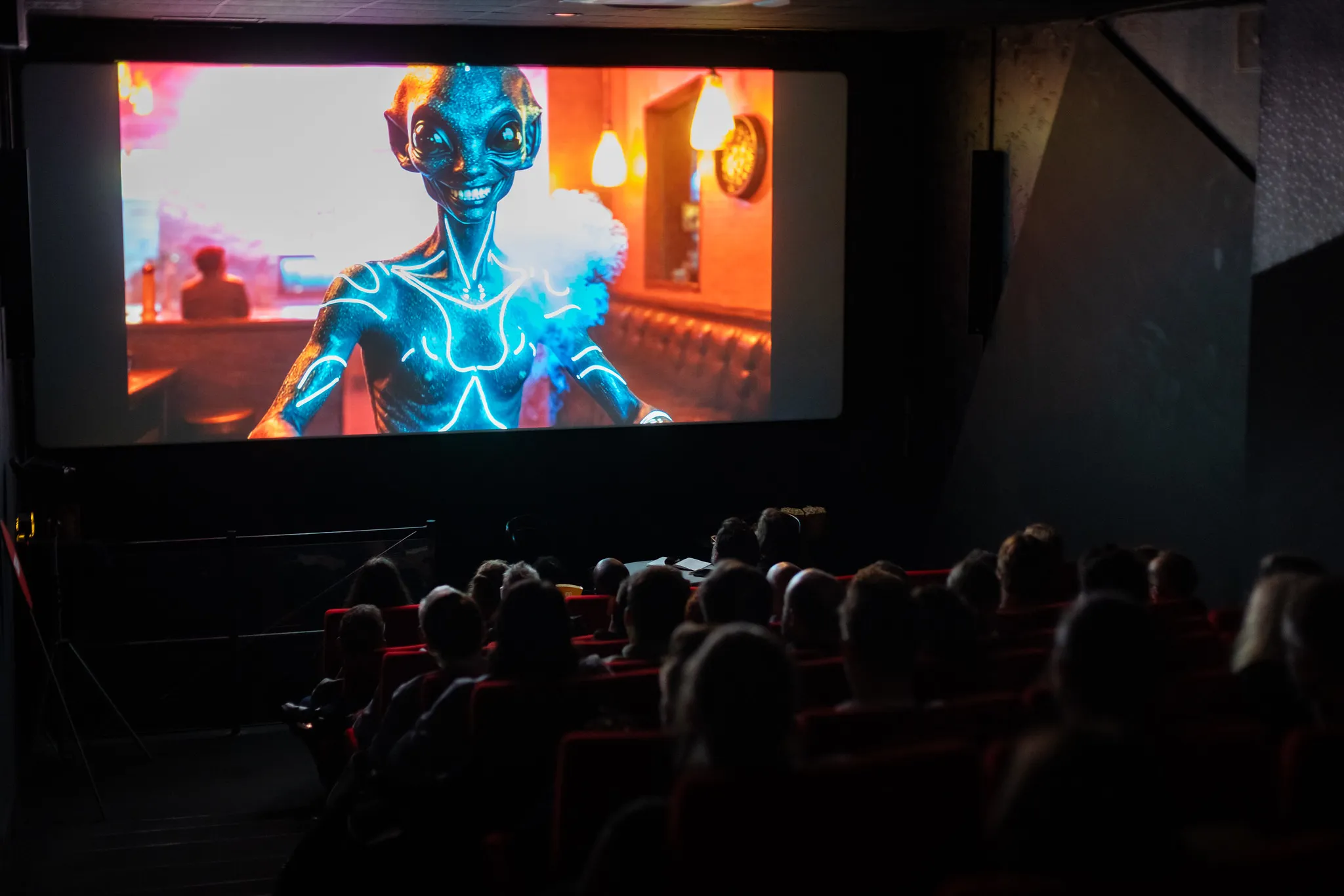 Audience watching a movie featuring a smiling blue alien with luminous body markings on a cinema screen.
