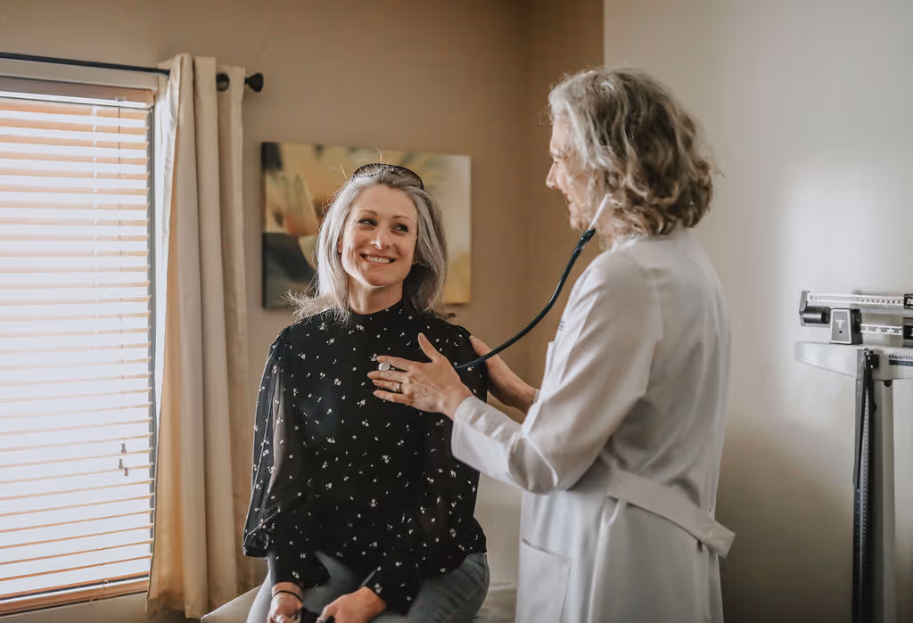 Dr. Libert listens with a stethoscope to a patients heart as she sits on the exam table. 