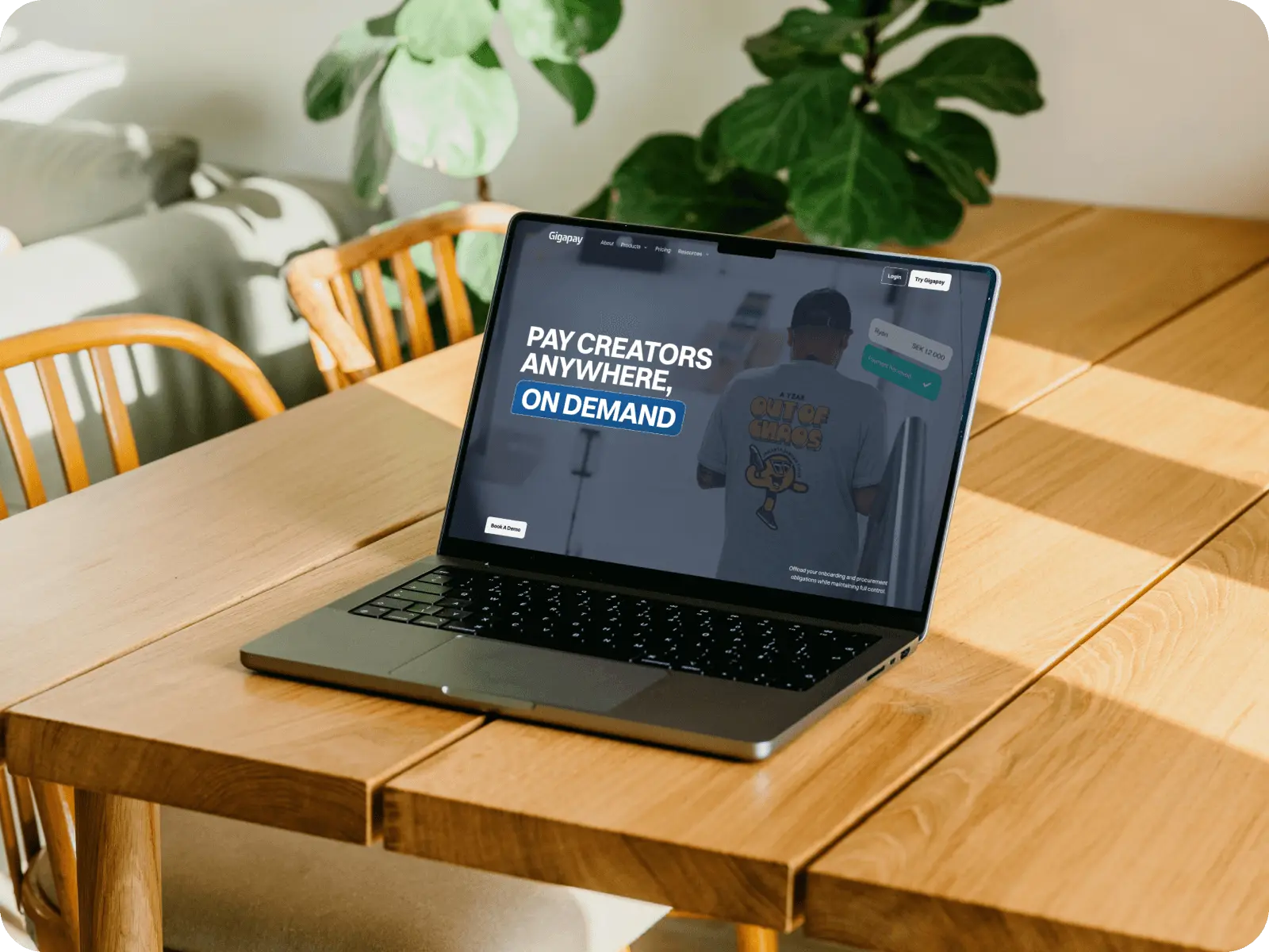 Laptop on wooden table displaying Gigapay website with text 'Pay creators anywhere, on demand'.
