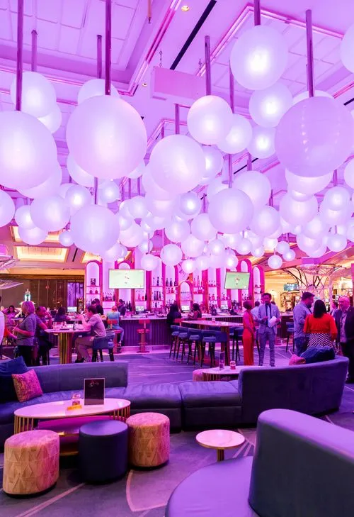 Stylish lounge bar illuminated with purple lighting during a private event; guests are mingling and seated, with modern furniture and a glowing ceiling installation above. Event planned and managed onsite by Stellify Events.