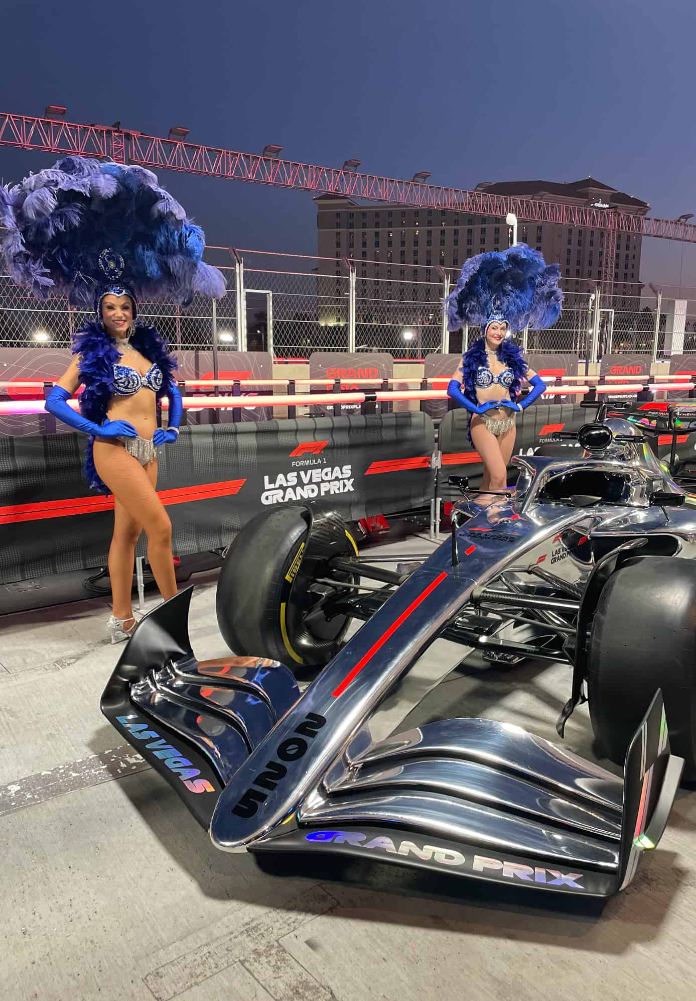 Two Las Vegas showgirls standing next to an F1 car at the Las Vegas Grand Prix Plaza.