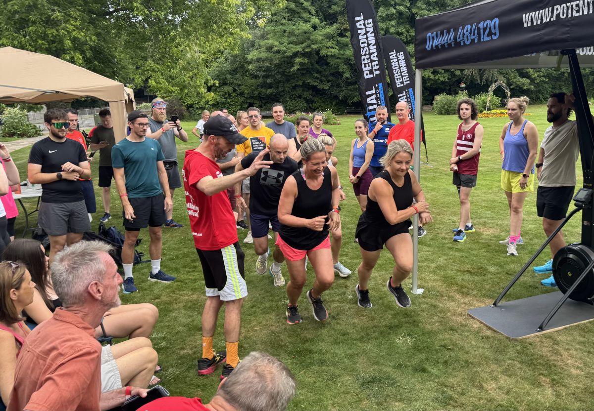 Runners taking on a team challenge on the grass, with a crowd cheering them on