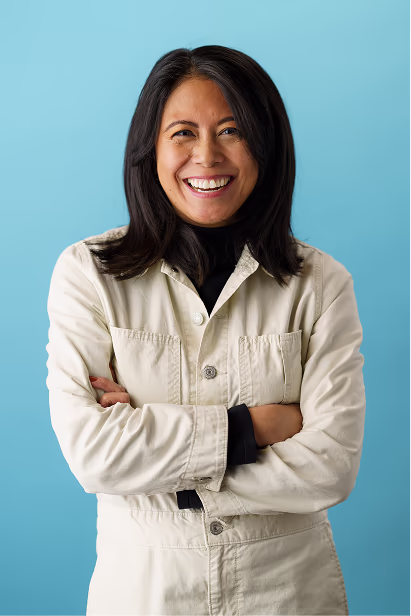 Notable team headshot of a woman in a cream jacket against a blue background