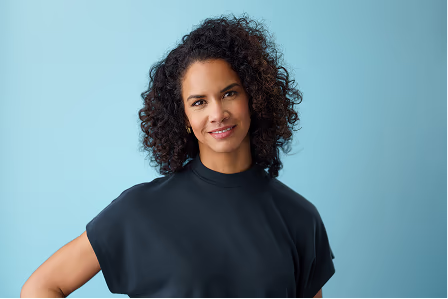 Notable team headshot of a woman with curly hair against a blue background