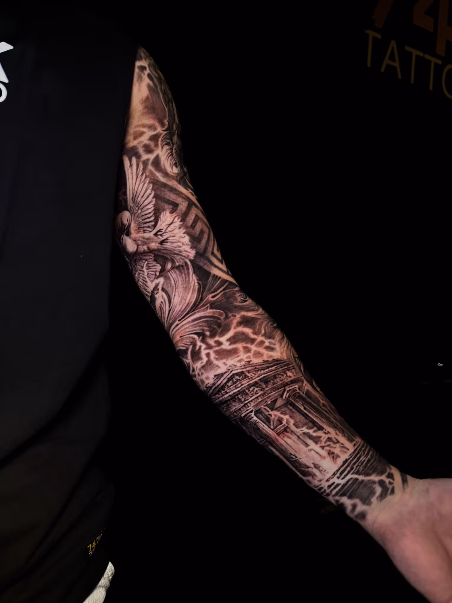 Arm sleeve tattoo featuring a flying dove, ornamental swirls, geometric patterns, and a classical temple with lightning effects.