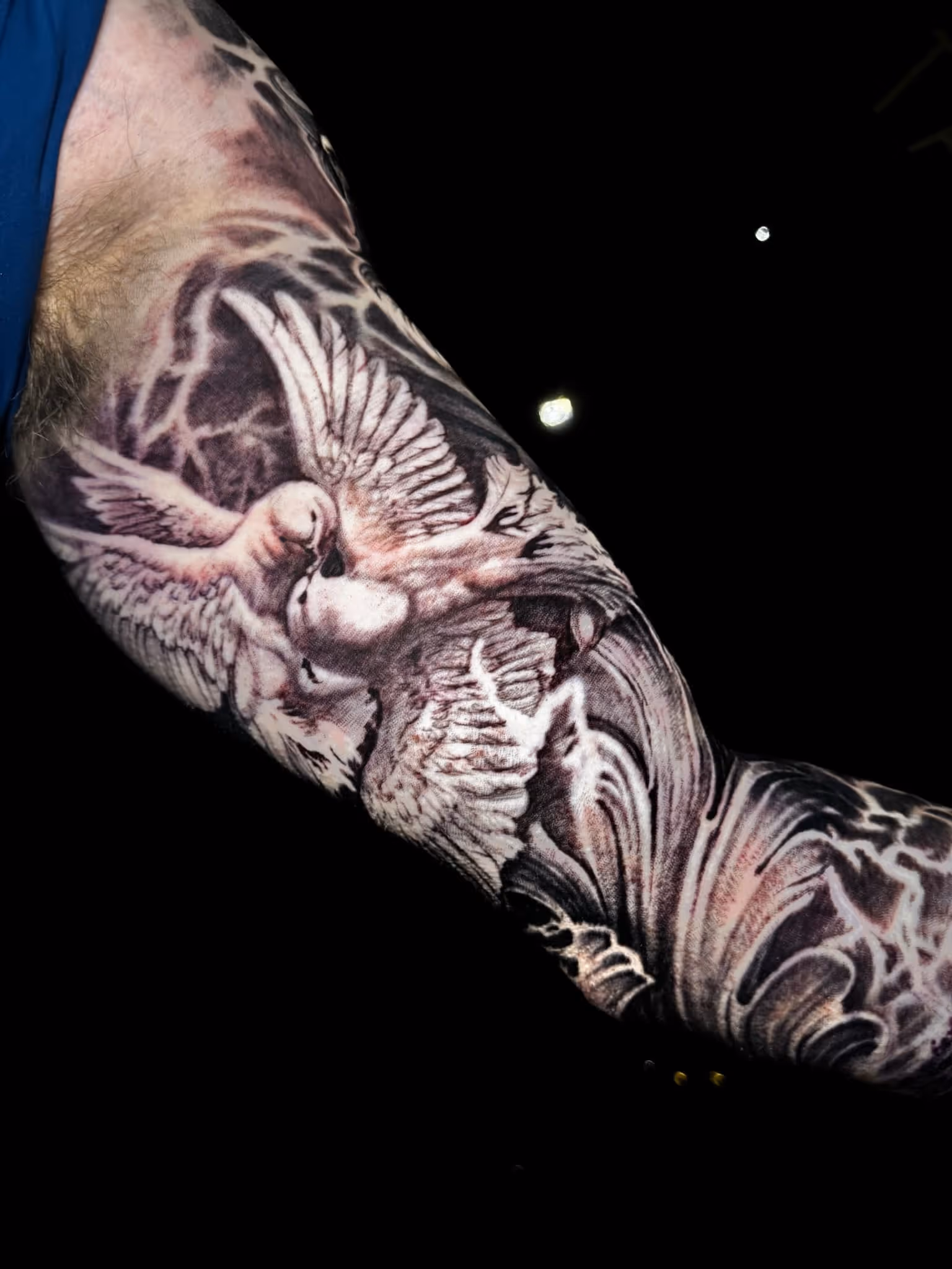 Tattoo of two doves with detailed wings surrounded by lightning patterns on a person's forearm.