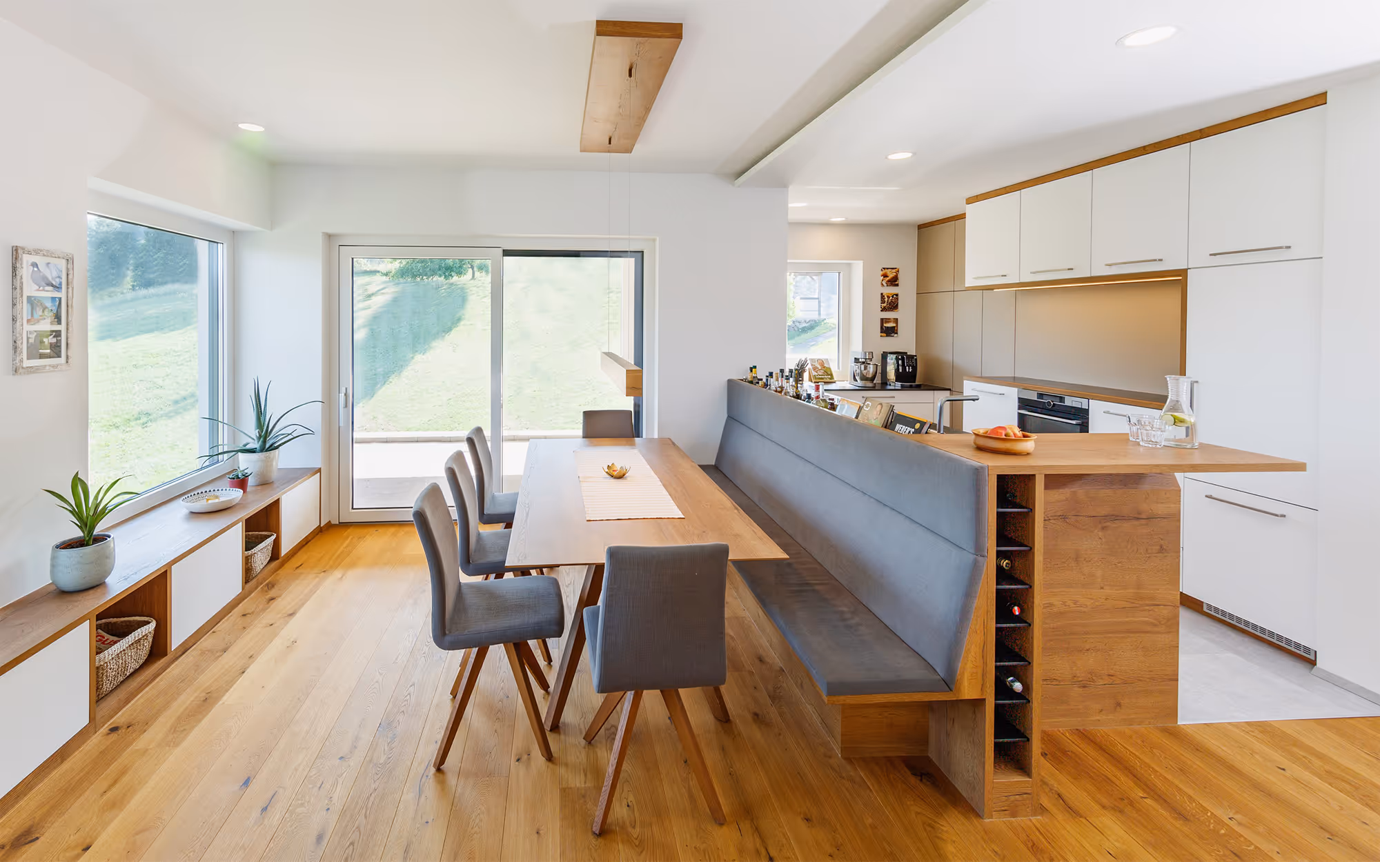Eine Küche mit großem angeschlossenen Esstisch in einem hellen Raum, gebaut von Design vom Grein in der Steiermark
