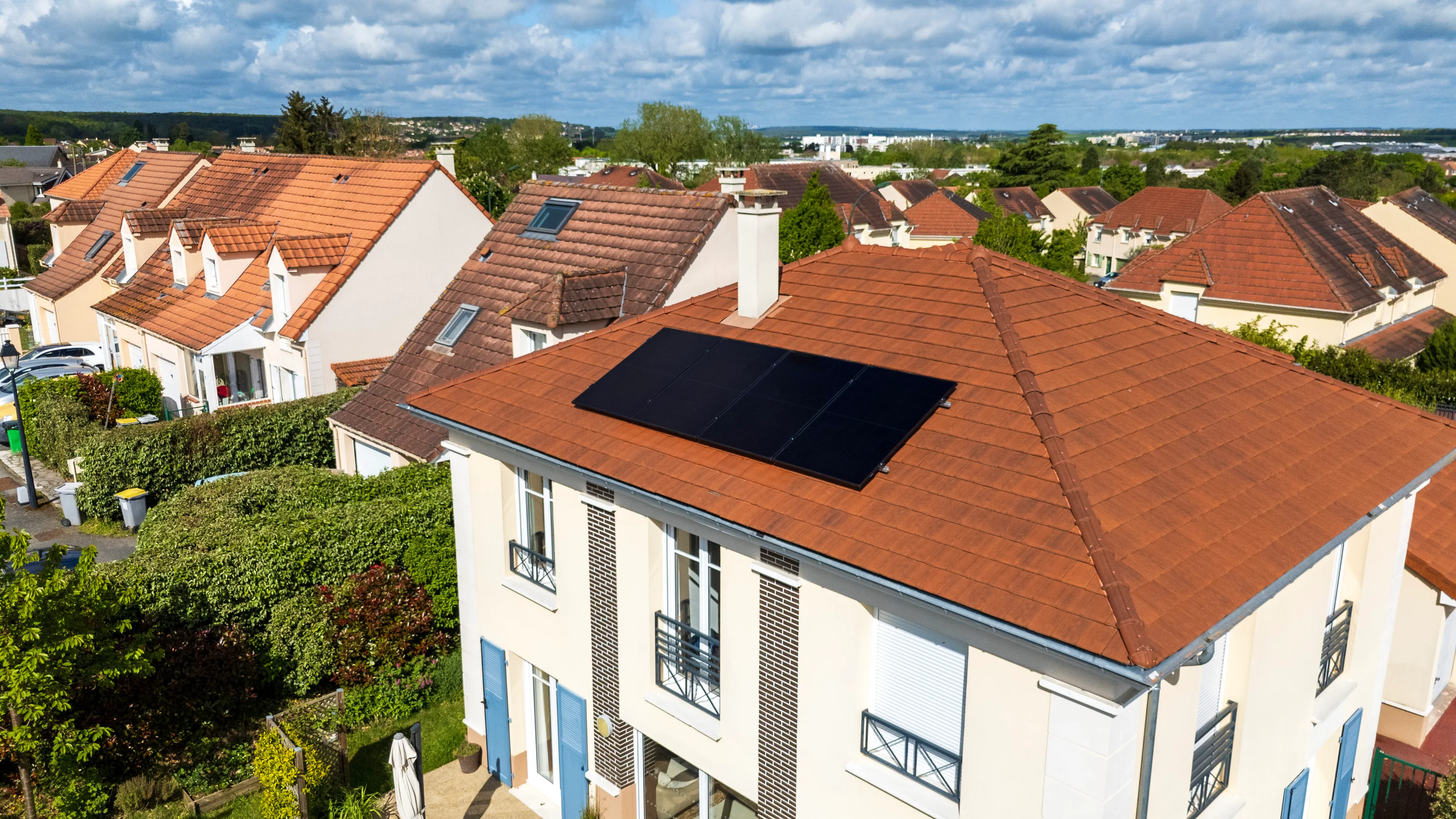 Maison avec toiture solaire sous un ciel nuageux, prise de haut.