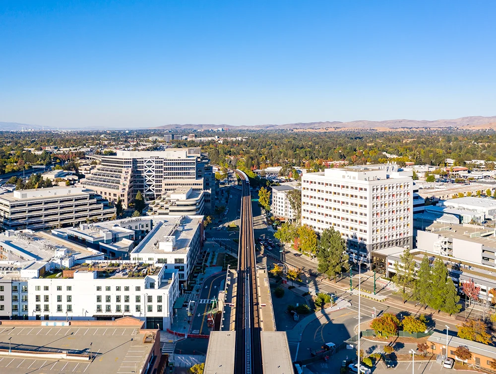 Drone photo above bart tracks in Walnut Creek, California with office building and a blue sky.