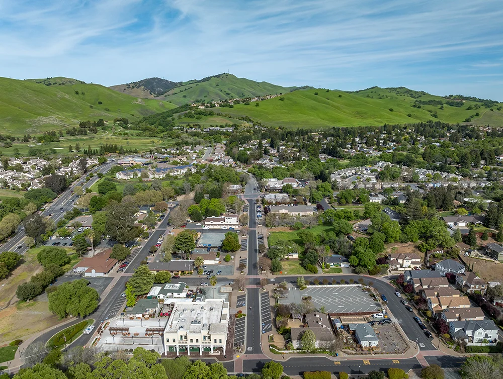 Drone photo over downtown Clayton, California with a blue sky, green hills and real estate