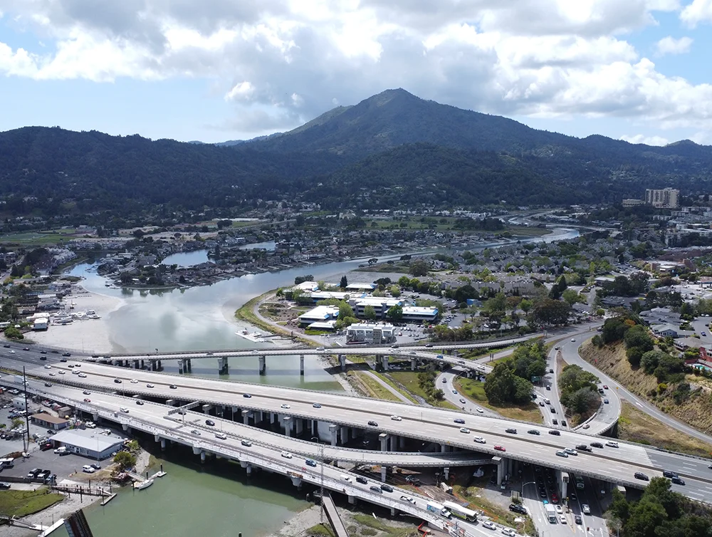 Aerial view of Mt Tamalpais, Corte Madera Creek and Highway 101 looking west toward bright, puffy clouds.