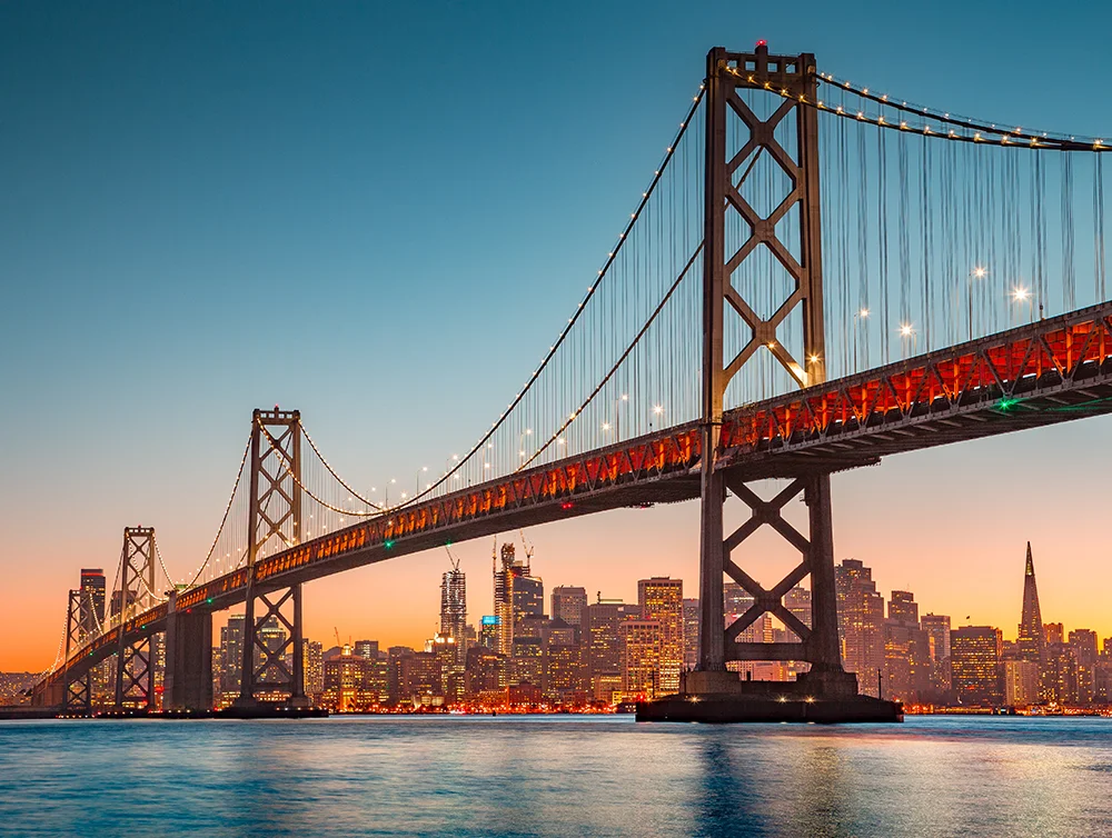 Classic panoramic view of San Francisco skyline with famous Oakland Bay Bridge illuminated in beautiful golden evening light at sunset in summer, San Francisco Bay Area, California, USA