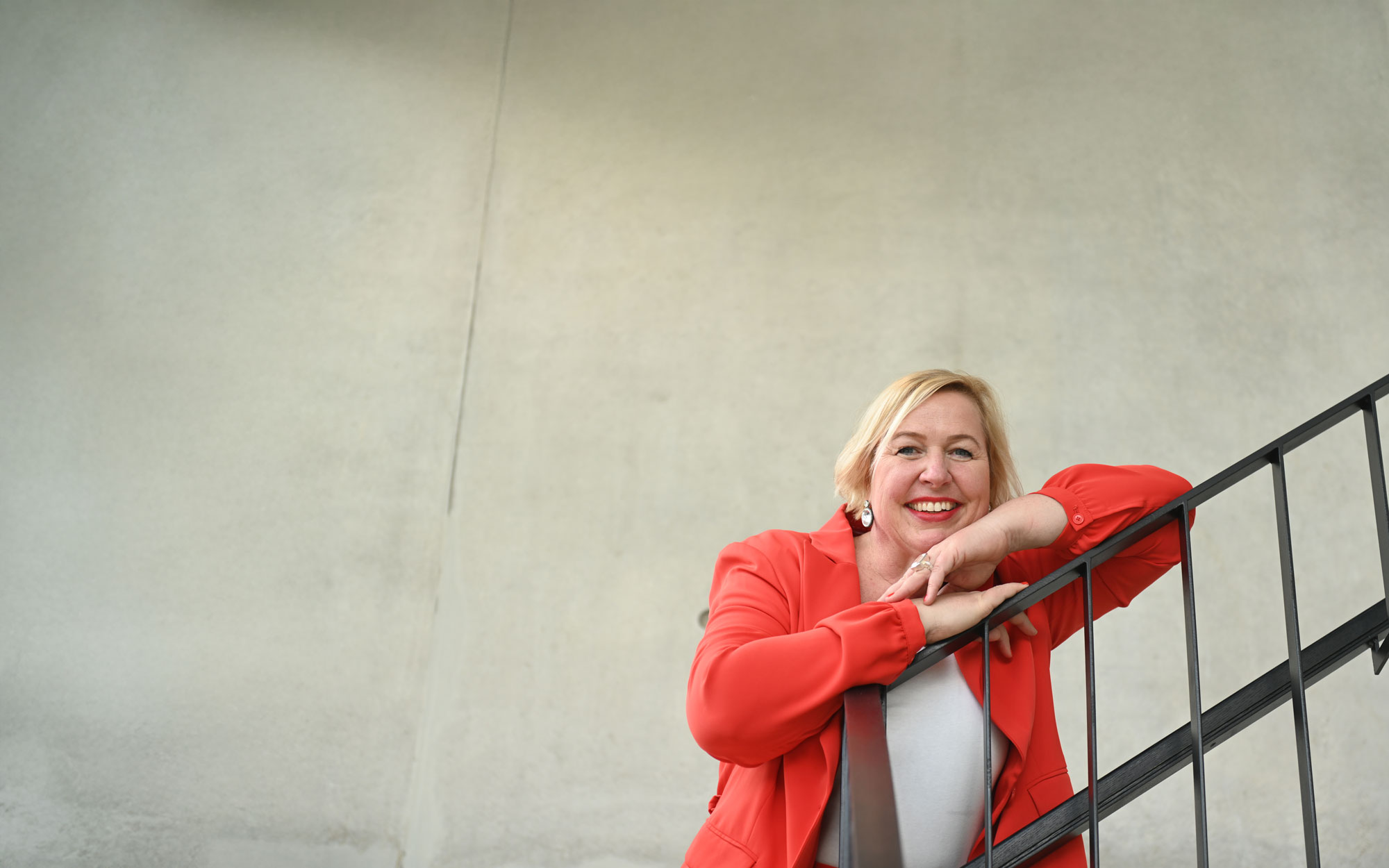 Frau mit rotem Blazer lehnt über ein Treppengeländer