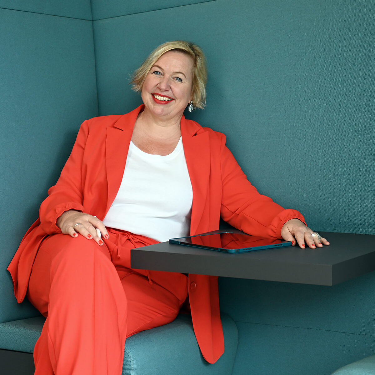 Frau mit rotem Blazer sitzt in einer grünen Besprechungsecke