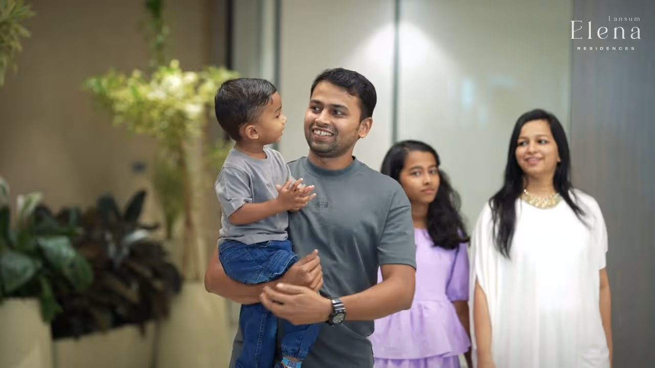 Smiling man holding a young boy with a woman and girl standing in the background indoors.