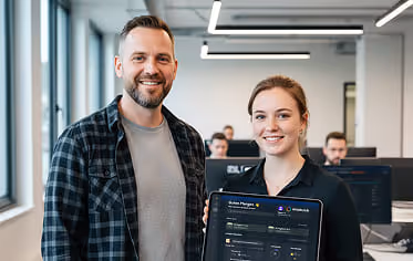 Ausbilder und Azubi stehen lächelnd mit einem Tablet in einem modernen Büro. Zeigt, wie einfache digitale Tools Trainern helfen, Zeit zu sparen und Azubis besser zu qualifizieren