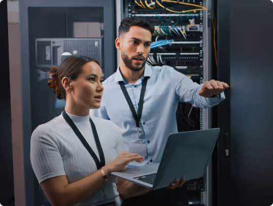 Azubi und Ausbilder arbeiten gemeinsam mit einem Laptop in einem Serverraum.