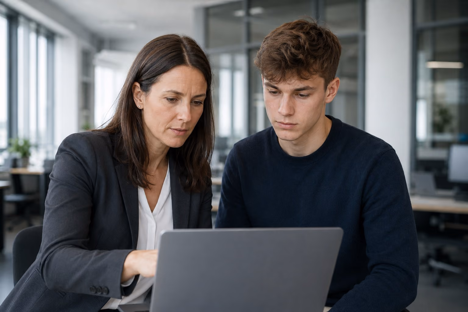 Ausbildungskoordinatorin und Azubi arbeiten gemeinsam am Laptop im Büro