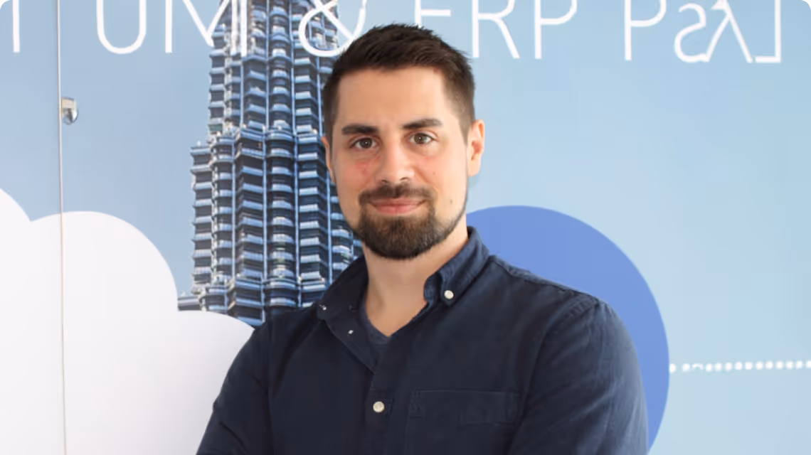 Mitarbeiter von HSO Enterprise Solutions steht mit verschränkten Armen vor einer blauen Wand mit Architekturmotiv und lächelt in die Kamera.