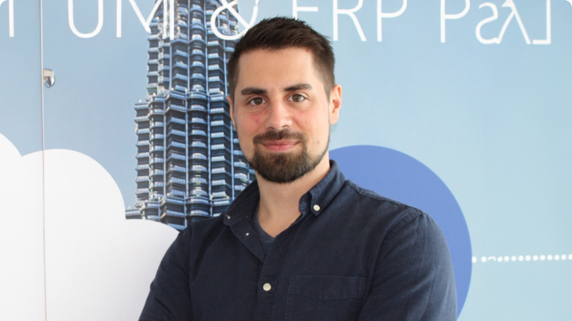 Mitarbeiter von HSO Enterprise Solutions steht mit verschränkten Armen vor einer blauen Wand mit Architekturmotiv und lächelt in die Kamera.