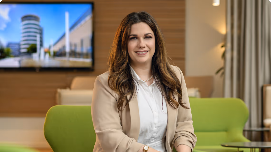 Mitarbeiterin der PSD Bank sitzt auf einem grünen Sofa, trägt einen beigen Blazer und lächelt in die Kamera.