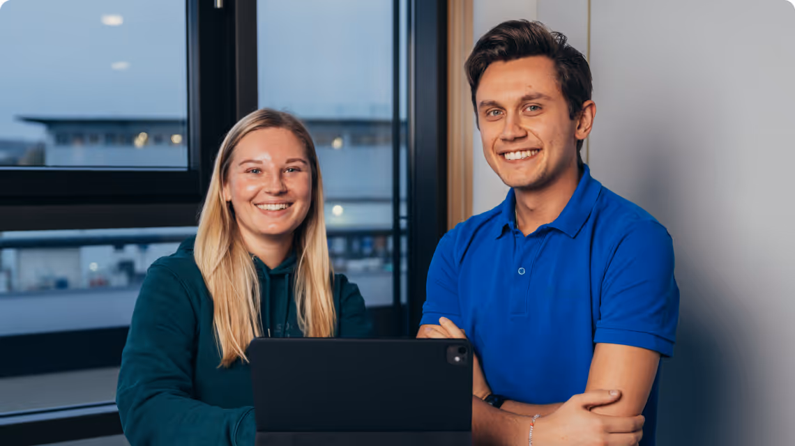 Zwei Auszubildende schauen gemeinsam auf ein Tablet und nutzen simpleclub in einem modernen Bürogebäude.