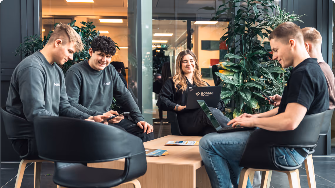 Gruppe von Auszubildenden sitzt in einem modernen, hellen Raum und nutzt simpleclub auf Laptops und Smartphones.