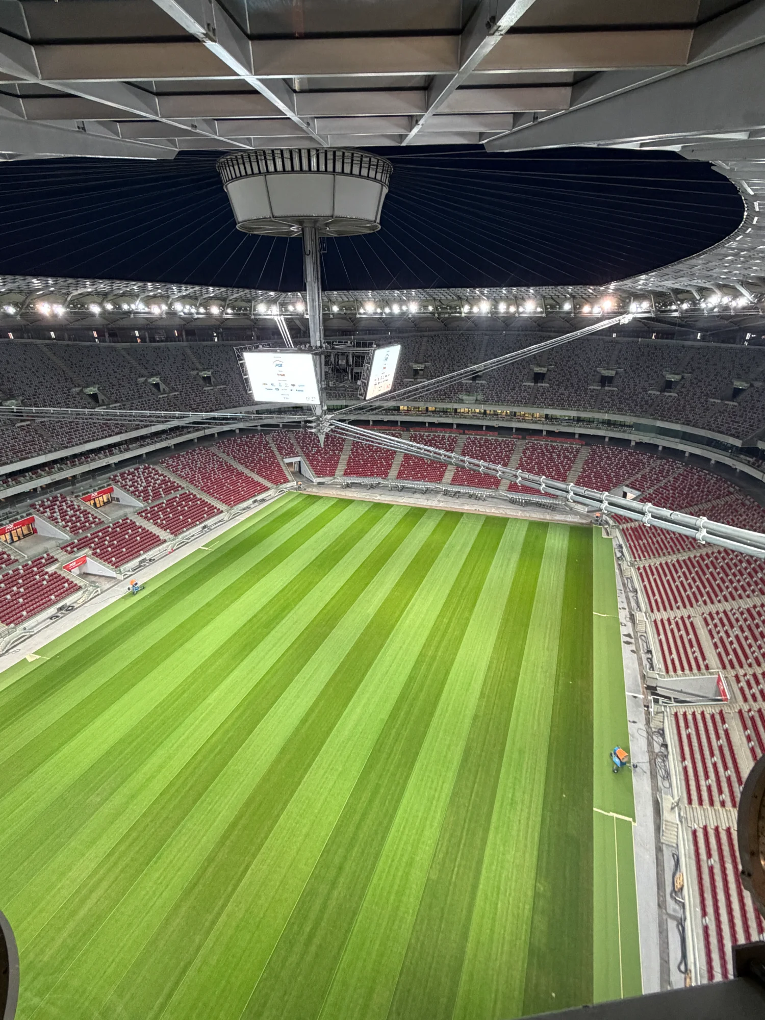 Szeroki kadr pustego stadionu PGE Narodowy, widoczny zielony murawa i czerwono-białe trybuny.